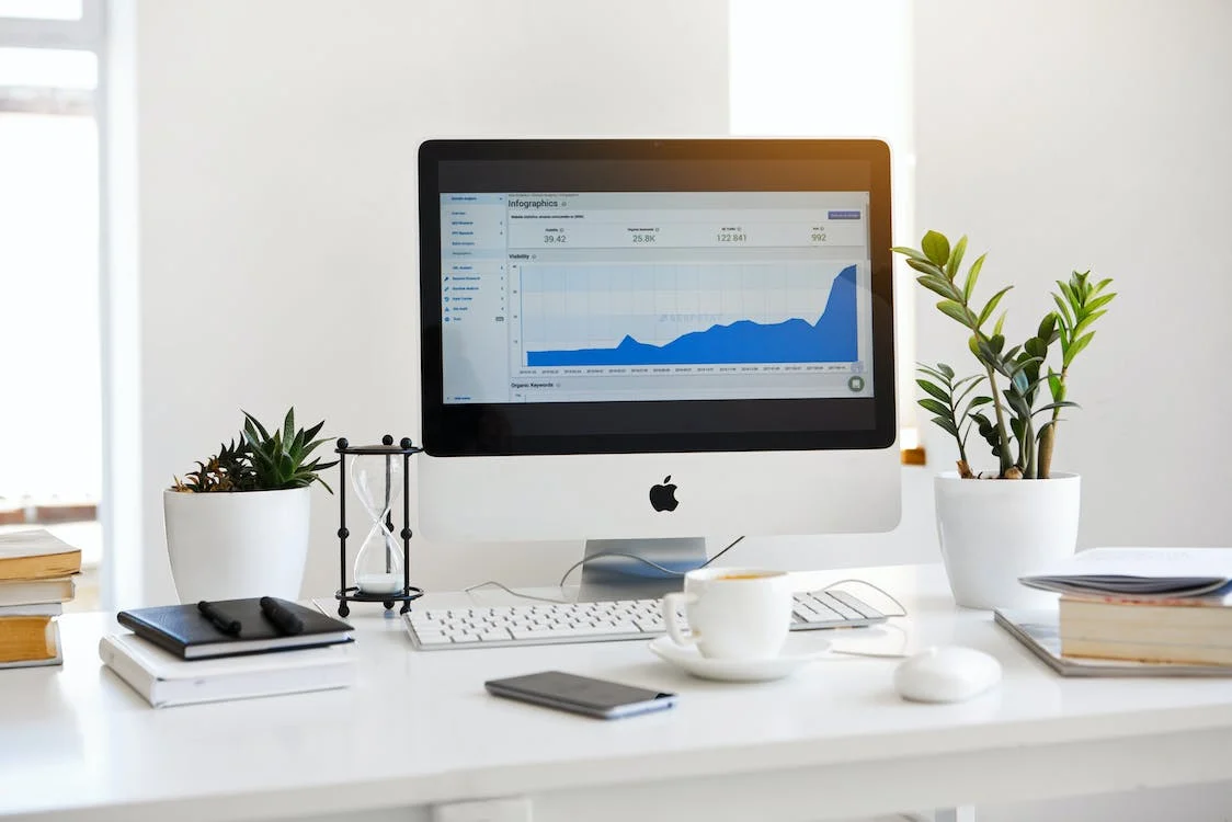 Une table comprenant des accessoires de bureau et un ordinateur iMac affichant un diagramme.